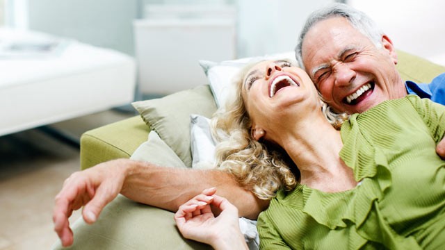 A picture of a male and female laughing on a couch